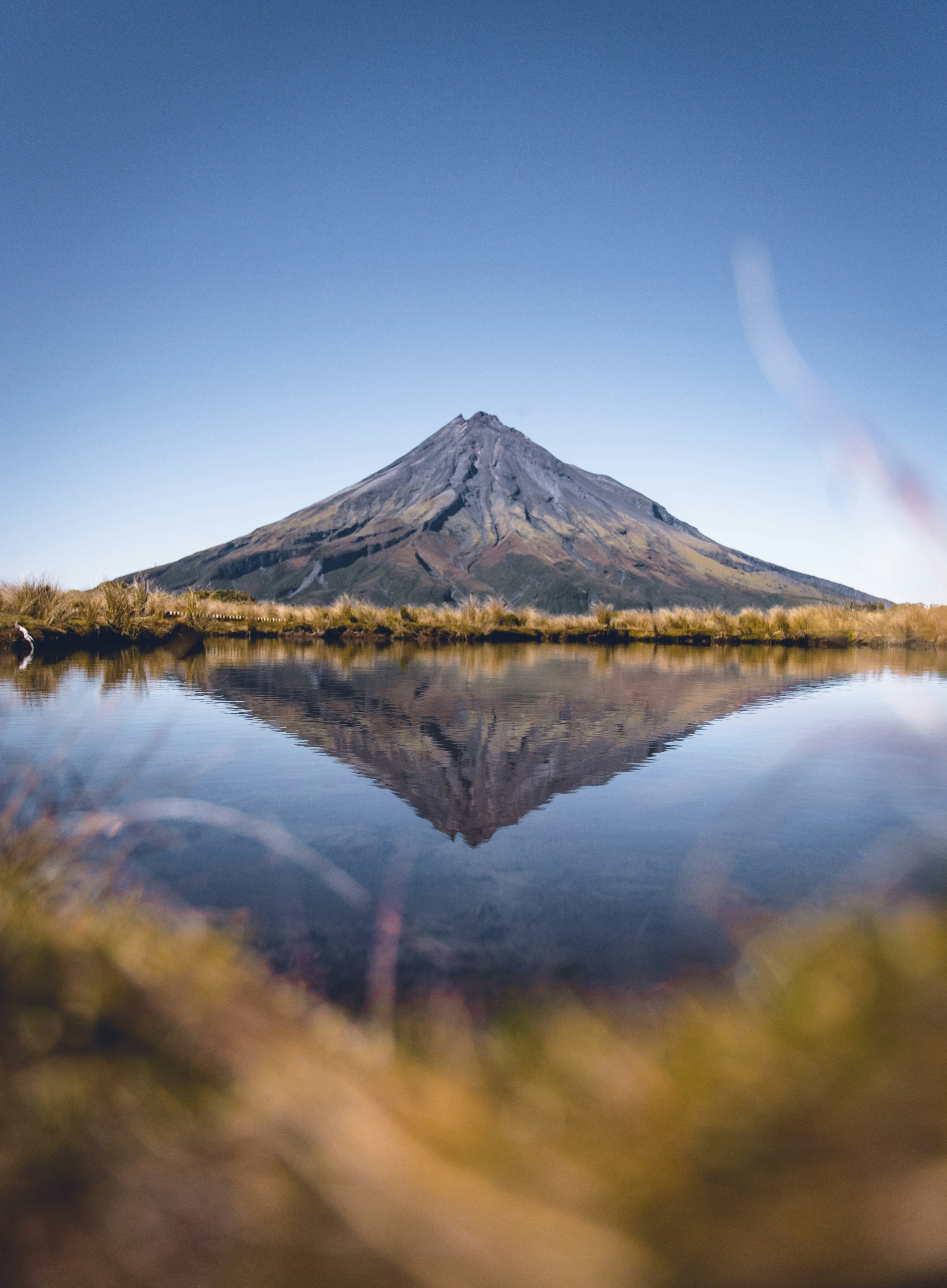 green and brown mountain beside lake under blue sky during daytime